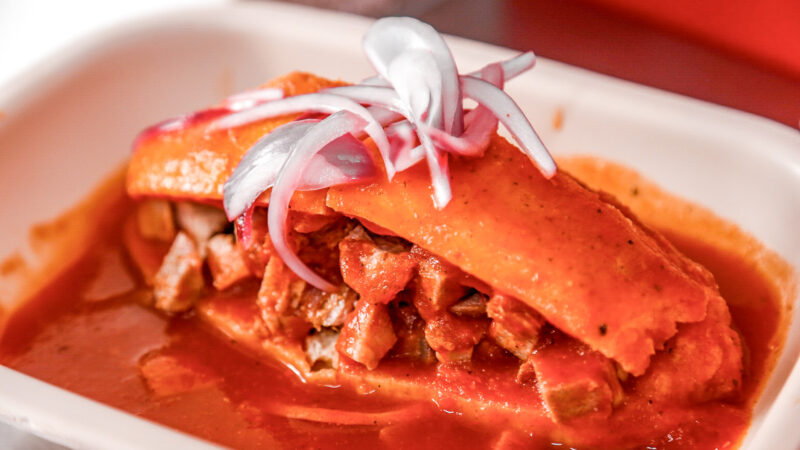 Torta ahogada de Guadalajara servida con salsa de jitomate, carnitas, cebolla encurtida y limón.
